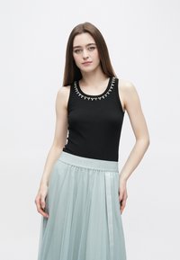 Μαύρο τοπ χωρίς μανίκια με στρογγυλή λαιμόκοψη διακοσμημένη με χάντρες, συνδυασμένο με μια αέρινη, φωτεινή γαλάζια τούλινη φούστα με ελαστική μέση με λογότυπο.