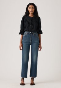 Μαύρο πουκάμισο με κουμπιά και υφασματική λεπτομέρεια, συνδυασμένο με ψηλόμεσα μπλε τζιν με ίσια γραμμή και ξεφτισμένο τελείωμα. Μαύρα σανδάλια με τακούνι.