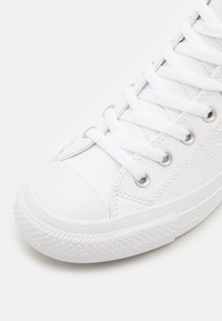 Zapatilla blanca con cordones, con parte superior de cuero liso, capucha de goma en la punta y suela de goma texturizada. Presenta ojales plateados y cordones planos.