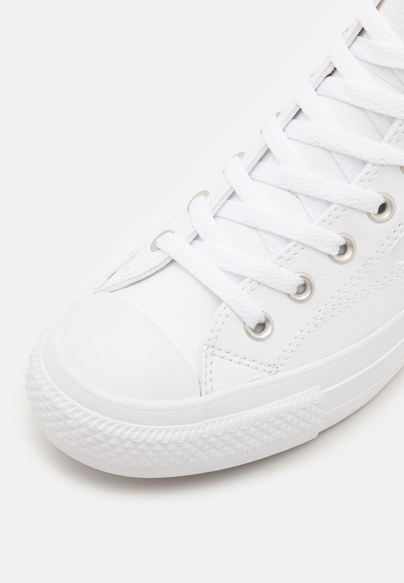 Zapatilla blanca con cordones, con parte superior de cuero liso, capucha de goma en la punta y suela de goma texturizada. Presenta ojales plateados y cordones planos.