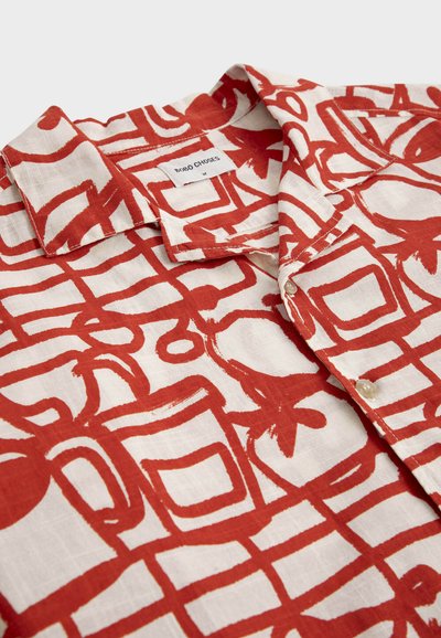 Chemise blanche boutonnée avec un motif abstrait géométrique et floral rouge, dotée d'un col et d'une étiquette de marque visible « Bobo Choses ».