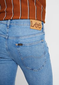 Ljust blå denimjeans med en läder Lee-logotyp i bakre midjan. Har klassisk fickdesign och subtila sömdetaljer.