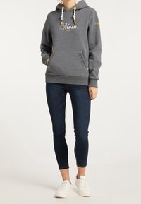 Grå hoodie med vit text "Moin", gula dragsnören och två framfickor. Bärs med mörka jeans och vita sneakers.
