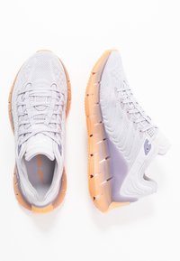 Jasnofioletowe trampki Reebok z tkaniny siateczkowej i gradientowymi pomarańczowymi podeszwami, widoczne z góry i z boku na białym tle.