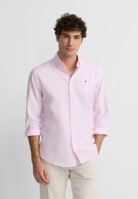 Camisa de botones rosa claro con mangas enrolladas, que presenta un pequeño logo en el pecho. Hecha de una suave tela de algodón.