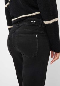 Jeans in denim nero con vita alta, tasche posteriori e etichetta con logo. Il tessuto ha una finitura opaca e una leggera elasticità.