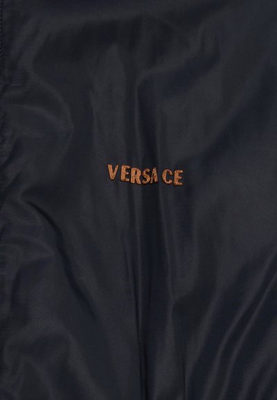 Μαύρο ύφασμα με τη λέξη «VERSACE» κεντημένη με καφέ κλωστή στο κέντρο.
