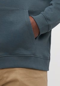Sudadera en azul oscuro con puños y bajo acanalados, que presenta un bolsillo frontal. Tejido texturizado, corte casual, combinada con pantalones caqui.