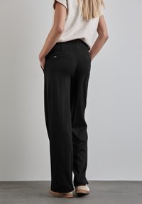 Pantalons larges noirs en tissu doux, avec une taille plate et des poches arrière, assortis à un haut simple de teinte neutre.