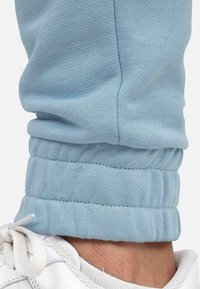 Lichtblauwe, aansluitende joggingbroek met geribbelde mouwen. Zacht, gestructureerd materiaal met een elastische tailleband, gecombineerd met zichtbare witte veters van sneakers.