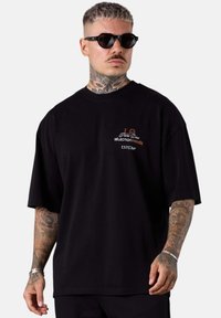 Schwarz Baumwoll-T-Shirt mit relaxter Passform, bedrucktem Text in Orange und Weiß. Kurze Ärmel und Rundhalsdesign.