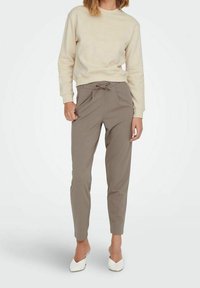 Felpa beige chiaro con scollo rotondo, abbinata a pantaloni jogger khaki a gamba stretta con vita elasticizzata e coulisse. Scarpe bianche.