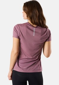 Short-sleeve athletic shirt in muted purple with a textured finish and a vertical white logo tag on the back. Paired with black leggings.
