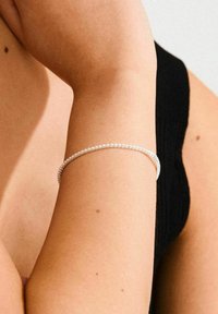 Silver bracelet with small beads, featuring a smooth, circular design. Worn on a tan arm, contrasting with a dark-colored garment.