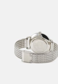 Montre en métal argenté avec un bracelet en maille tissée, boîtier rond et couronne ronde simple. Présente une finition lisse et polie ainsi qu'une fermeture à clip.