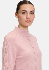 Rosa gestrickter Pullover mit hohem Kragen und Zopfmusterdetails an den Ärmeln, der eine weiche Textur und eine figurbetonte Silhouette bietet.