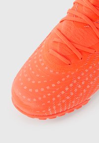 Lyseorange fodboldstøvle med en tekstureret overdel med hvide prikker, flade snørebånd og en gummisål designet til greb.