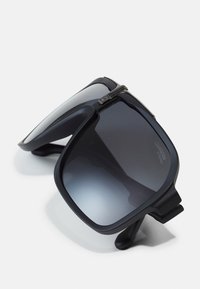 Ochelari de soare supradimensionați, de culoare neagră, cu lentile întunecate în degrade, finisaj mat și un detaliu unic de tip clip-on pe ramă. Design robust și formă unghiulară.