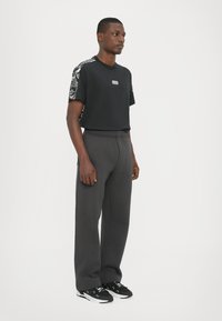 Black t-shirt with patterned sleeves, gray sweatpants, and black sneakers. The fabric appears soft with an elastic waistband and logo detail.