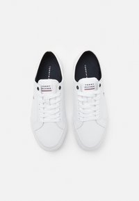 Weiße Leinenschuhe mit rundem Zehenbereich, Schnürsenkelverschluss vorne und Markenlogo auf der Zunge. Schwarze Innensohle sichtbar, mit dezenten Nahtdetails.