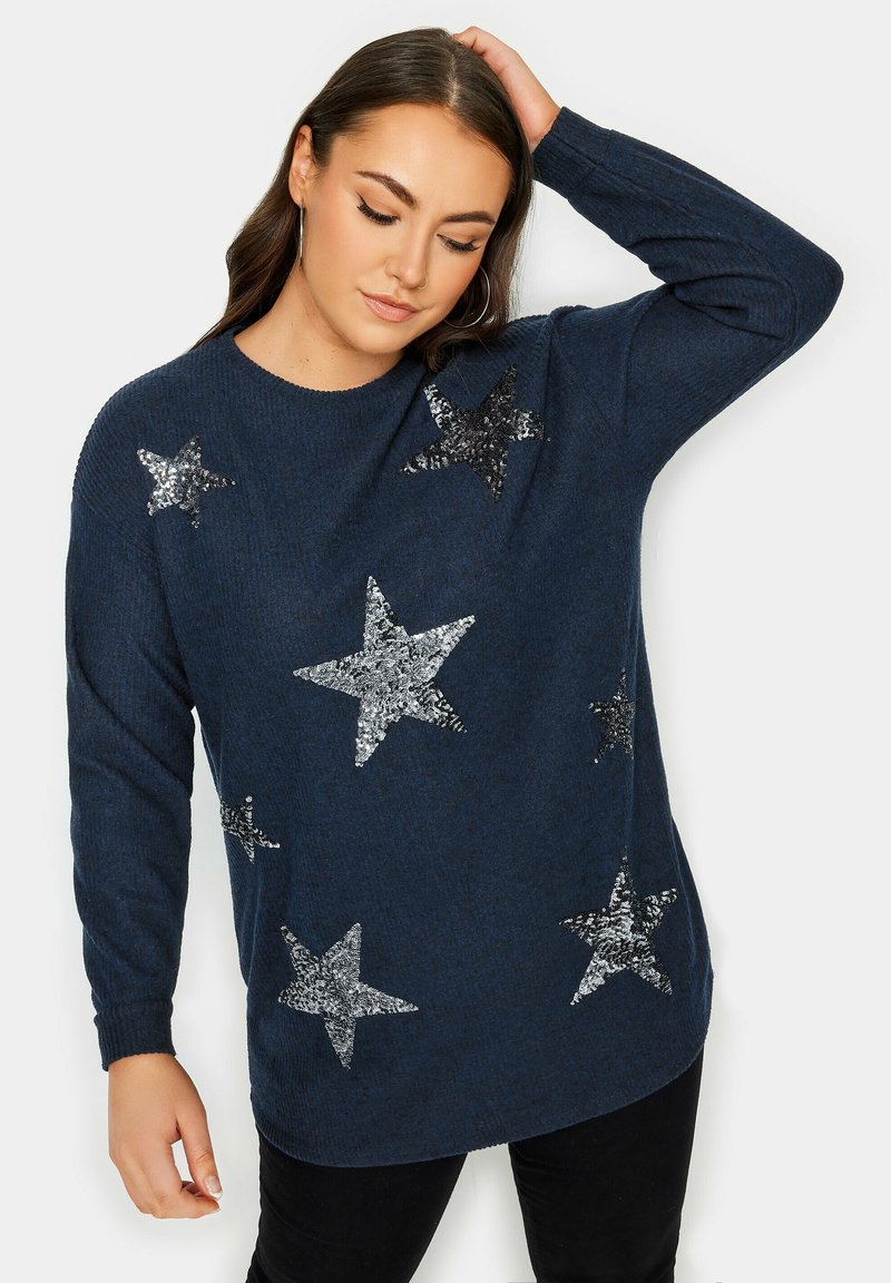 Marinblå stickad tröja med silverfärgade paljetter i stjärnmönster, rundad halsringning och långa ärmar. Materialet verkar mjukt och har en texturerad yta.
