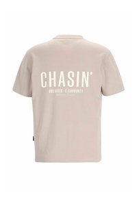 Lyse beige t-shirt lavet af blødt bomuld, med rund hals og korte ærmer. Tekst trykt i hvid på ryggen inkluderer "CHASIN'" og andre detaljer.