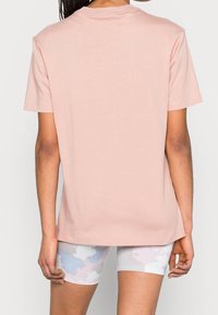 Kort rosa bomullströja med rund hals och korta ärmar, bärs över ljusa mönstrade shorts. Slät textur, avslappnad passform och enkel design.