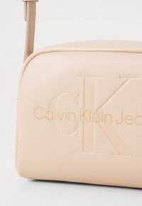 Borsa Calvin Klein Jeans, materiale sintetico beige, forma rettangolare, logo in rilievo, texture liscia, tracolla slim regolabile.