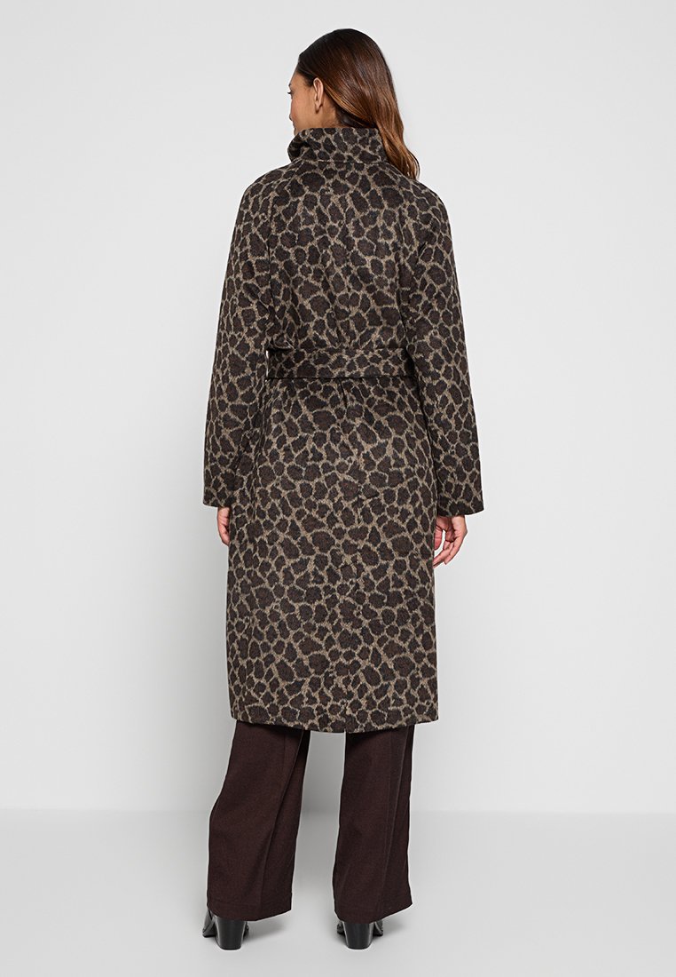 Donna che indossa un cappotto leopardato marrone e nero di lunghezza intermedia con colletto alto, abbinato a pantaloni in fresco di roccia marroni a gamba larga e scarpe nere, girata di spalle.