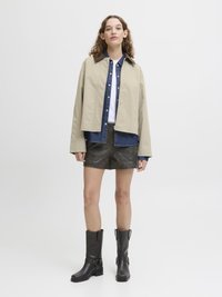 Beige kort jakke, denim lagdelt skjorte, hvit T-skjorte, brune shorts og svarte knelang støvler. Enkelt design, avslappet passform og teksturert stoff.