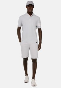 Svetlošedé polo tričko s kontrastným golierom a pásmi na rukávoch, spárované s rovnakými šortkami. Biele tenisky dopĺňajú outfit.