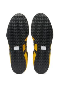 Černé a žluté tenisky s texturovanou gumovou podrážkou s kruhovými vzory. Design obsahuje diagonální pruh jako akcent na straně.