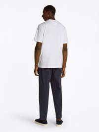 White short-sleeve t-shirt, relaxed fit, paired with dark checkered trousers and navy sneakers. Simple design with crew neckline.