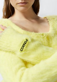 Žuta krznena pulover blaga mekane teksture, s okruglim izrezom, zatvaranjem na gumb i crnom oznakom "PINKO" sprijeda.