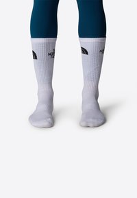 Calcetines blancos de longitud hasta la rodilla, hechos de tela tejida, con texto de logo negro en la parte delantera y una textura acanalada en la parte superior.