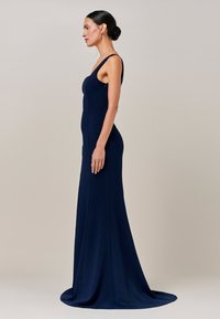 Večerna obleka mornarsko modre barve s prilagojeno silhueto, scoop izrezom in dolžino do tal. Ponaša se z gladkim materialom in minimalnimi okraski.