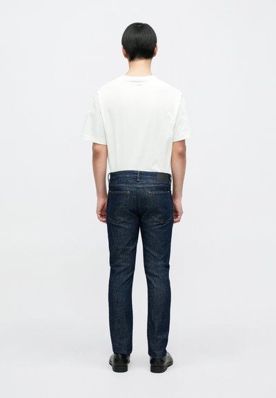 Chemise blanche à manches courtes avec un col rond, associée à un jean bleu foncé. Le jean présente une coupe ajustée et des poches arrière.