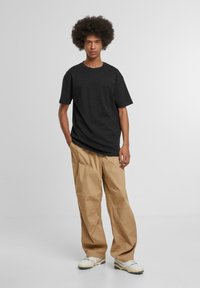 Black cotton t-shirt with short sleeves, paired with beige wide-leg pants featuring cargo-style pockets and white sneakers.