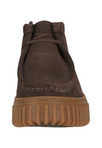 Bruine suède enkellaarsjes met een ronde neus en een beige rubberen zool met geribbelde textuur, vetersluiting en contrasterende stikseldetails.