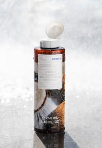 Amber kunststof fles met een witte flip-top dop. Het etiket toont "Herstellende Lichaamsreiniger" met kokosnoot afbeeldingen. 250 mL, 8,45 FL. OZ.