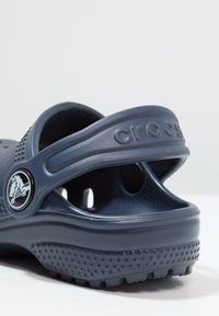 Scarpe slip-on Crocs di colore blu navy, in gomma testurizzata, con un accento di bottone logo, cinturino regolabile e fori di ventilazione per la traspirabilità.