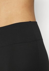 Leggings de fitness noirs en tissu lisse et extensible ; taille haute avec un design de coutures plates ; texture mate et sans motifs visibles.