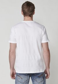 T-shirt bianca a maniche corte con un motivo a righe texturato, colletto rotondo e vestibilità rilassata, abbinata a jeans blu.