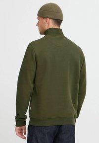 Grønn hettegenser med høy krage, ribbede mansjetter og kant. Myk tekstur, minimalistisk design, sammen med en matchende strikket lue.