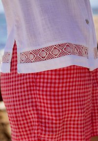Biała lniana koszula z koronkowymi detalami na dole, zestawiona z czerwono-białymi spodniami w kratę gingham, prezentująca teksturowany, swobodny wygląd.