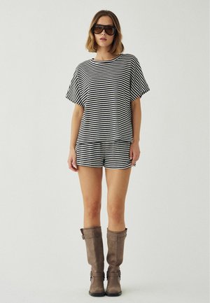 Kvinde iført sort-hvidt stribet kortærmet top og matchende shorts, brune knæhøje støvler og store mørke solbriller.