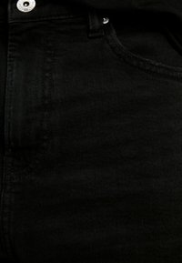 Svarta denimjeans har en klassisk femficksdesign med en slät yta, lätt stretch och en synlig knappstängning i midjan.