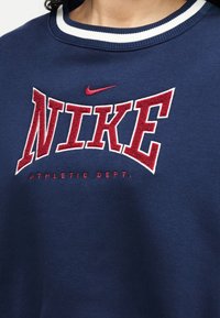 Primer plano de una sudadera azul marino con el logo de Nike en rojo y blanco y el texto rojo "ATHLETIC DEPT." debajo del nombre de la marca.