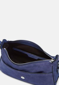 Sac bandoulière en daim bleu avec fermeture à glissière, poche intérieure et quincaillerie en argent. La surface a une texture lisse avec des coutures accentuées.