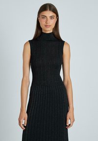 Abito nero a coste con collo alto e design senza maniche. Presenta un corpetto aderente e una gonna a ruota con pieghe.